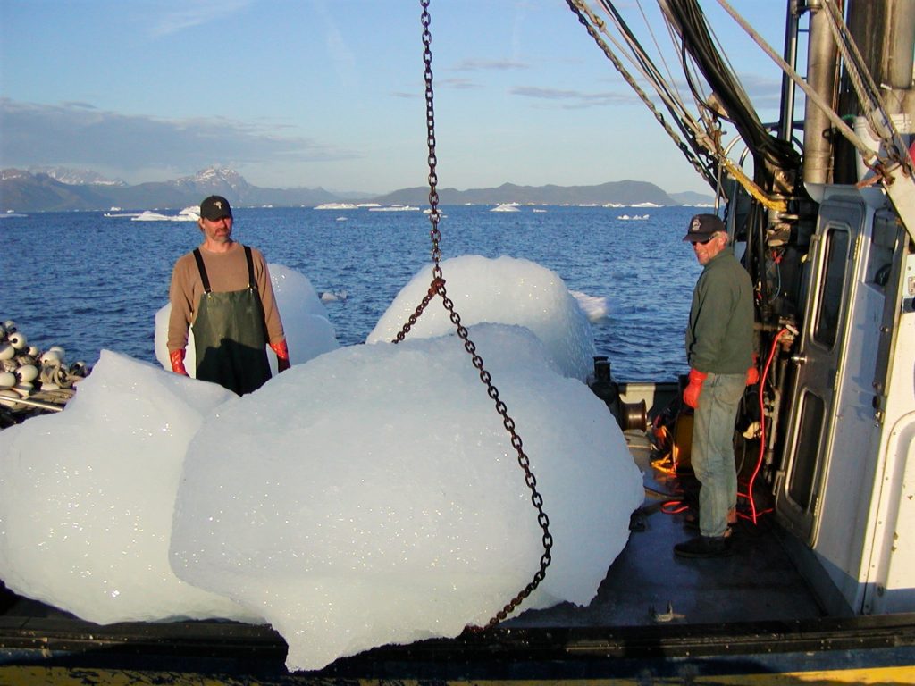 Two workers use a crane to life chunks of glacier ice on to a boat