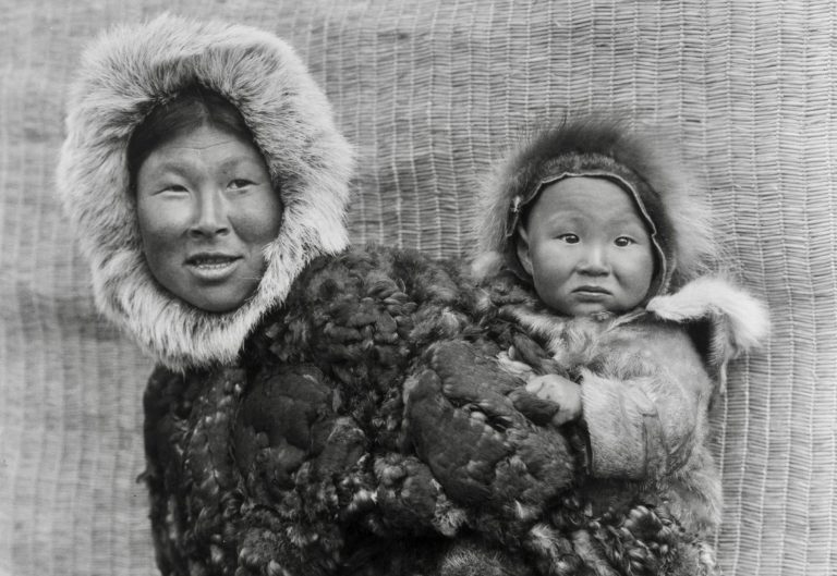 Nunivak woman wearing a parka and carrying a young child on her back