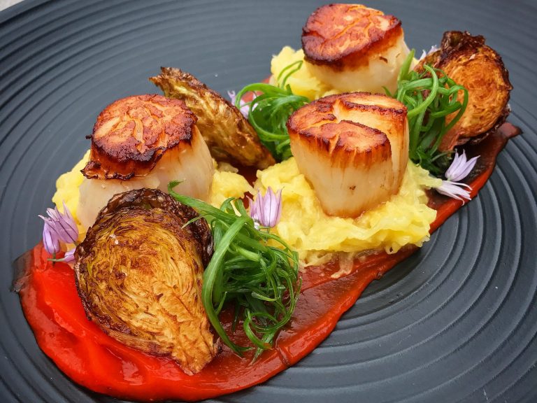 A gray plate with beautifully presented scallops, greens