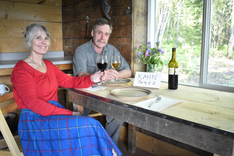 Steve Kahn and Anne Coray pose and cheers wine at a cabin table