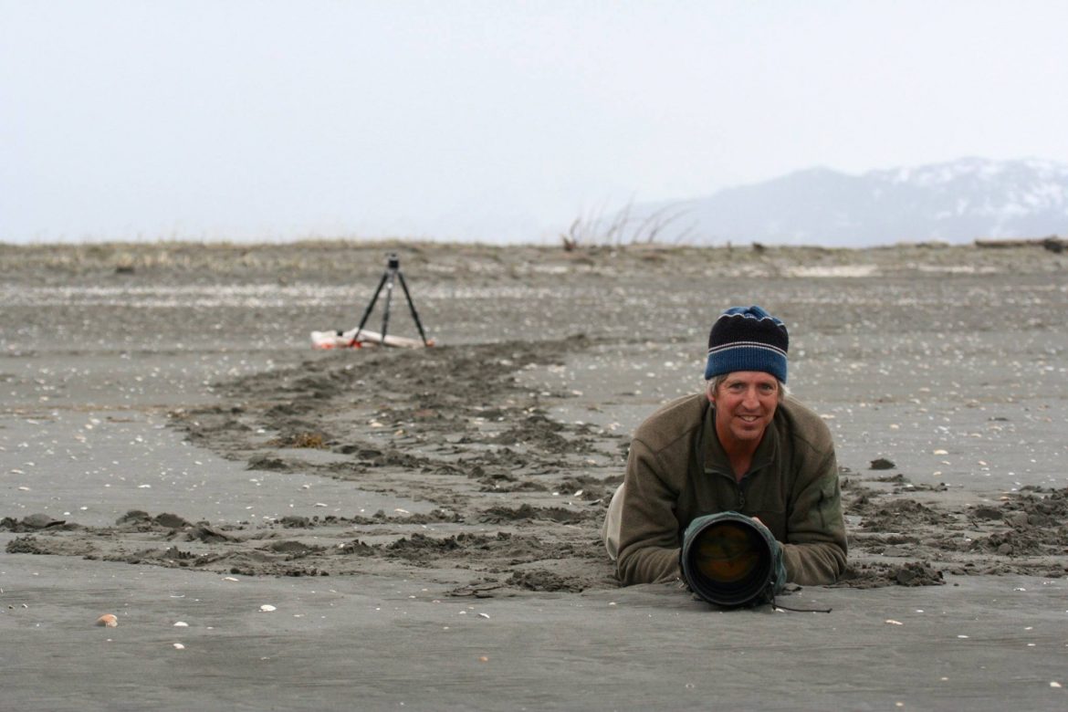 Wildlife photographer Milo Burcham lying in the sand with camera