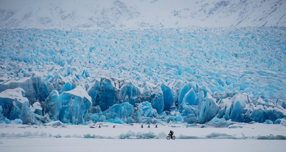 Fat-bikers bike across snow and ice at the toe of the Knik Glacier