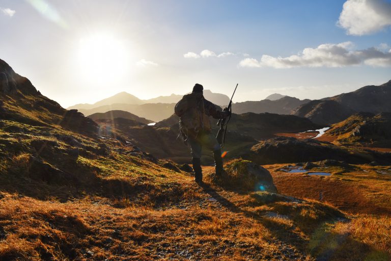Caribou Hunting in Adak. Hunter backlit by sun looking over mountains