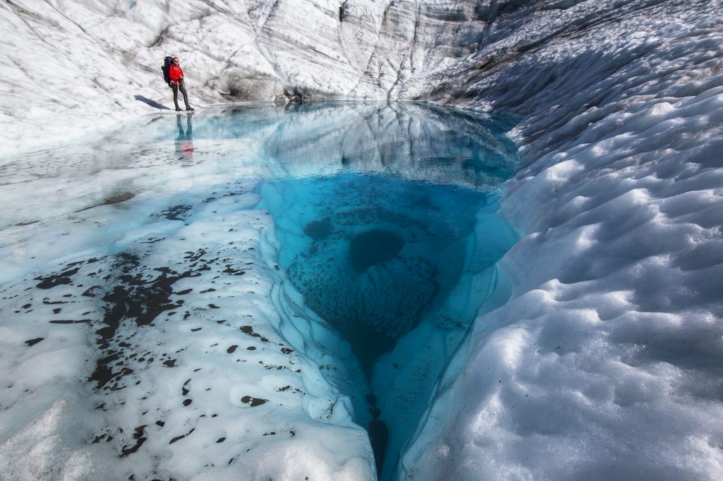 Hiker stands by a pool of water on glacial surface