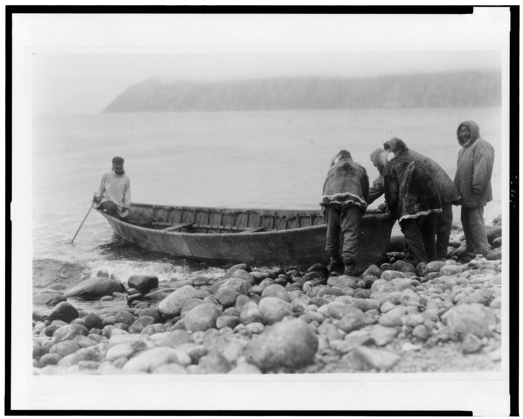 Black and White image men in parkas launching boat from rocky beach