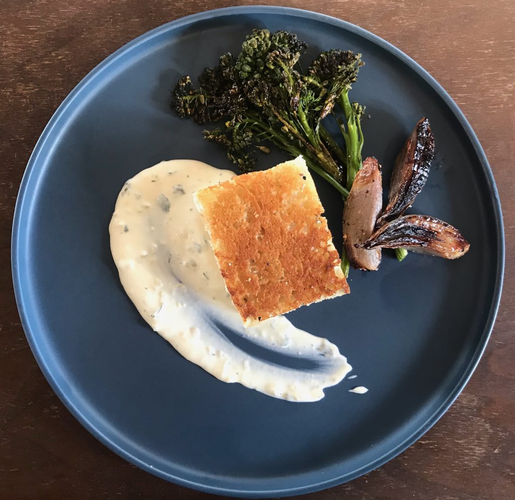 finished halibut en croute on black plate with sauce and vegetables