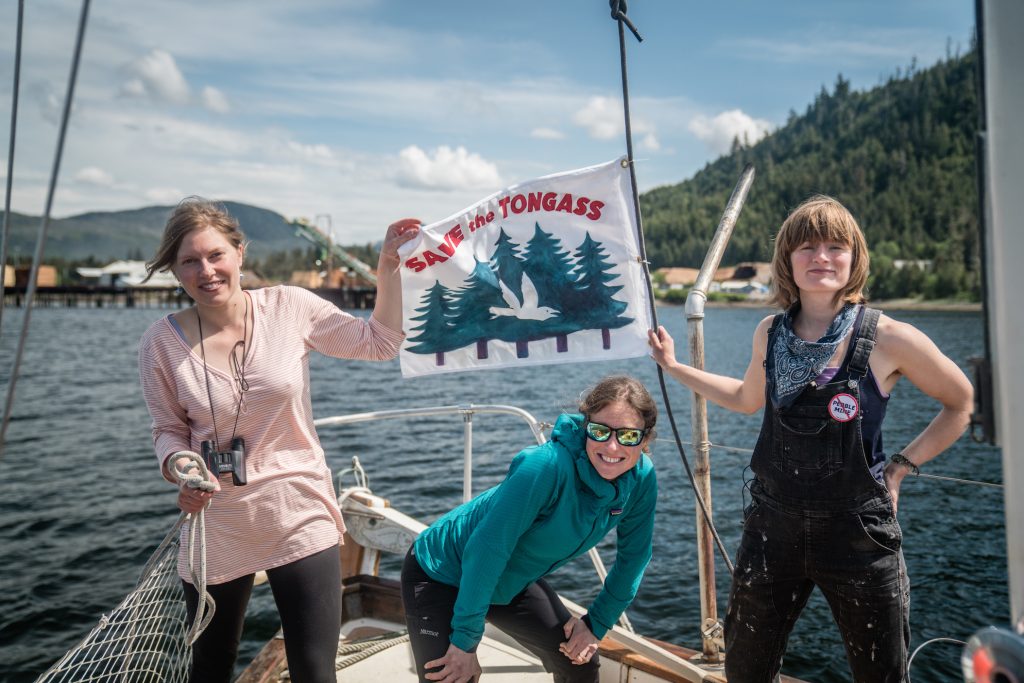 Natalie Dawson posing with two other women on a boat holding a small flag that says Save the Tongass