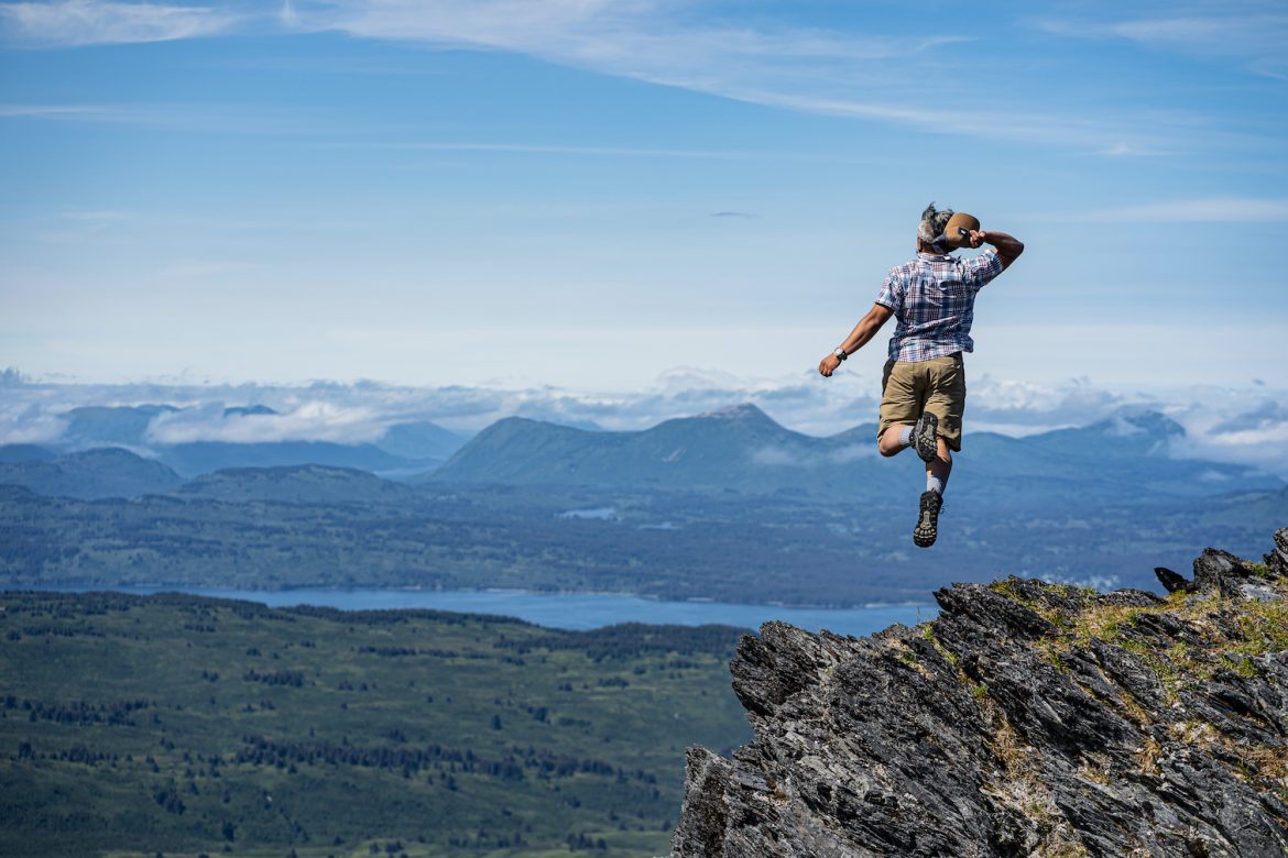 A hiker jumps on the summit of Sharatin Mountain as part of a Kodiak hiking challenge