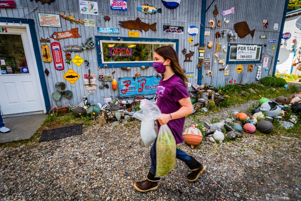 A girl carries a plastic bag full of spruce tips in front of a store.