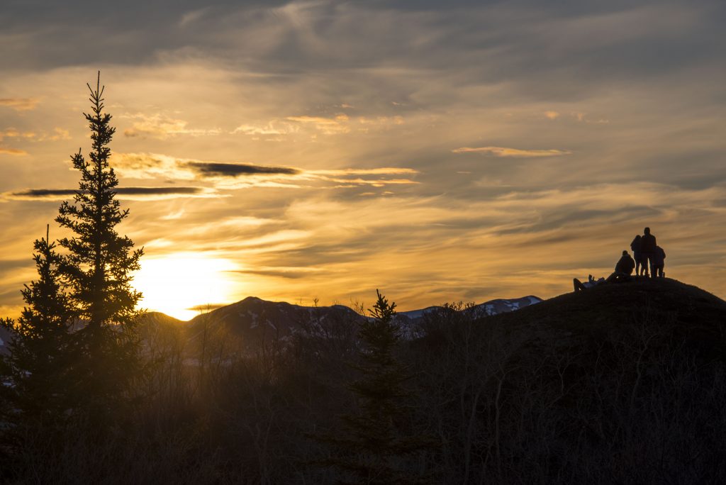Setting sun creates a silhouette of mountains and trees on the horizon.