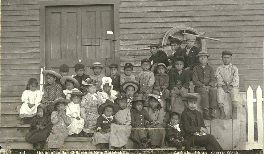 black and white photo of children lined up in front of wooden building