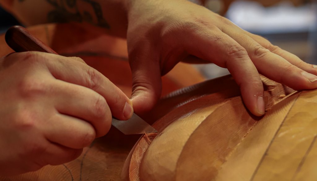 Close on Tsimshian artist David R. Boxley's hands and a tool as he carves.