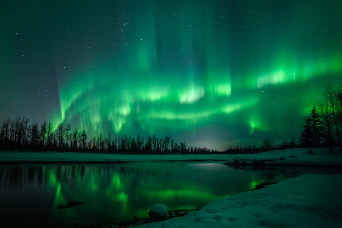 Green aurora over clear night sky above lake