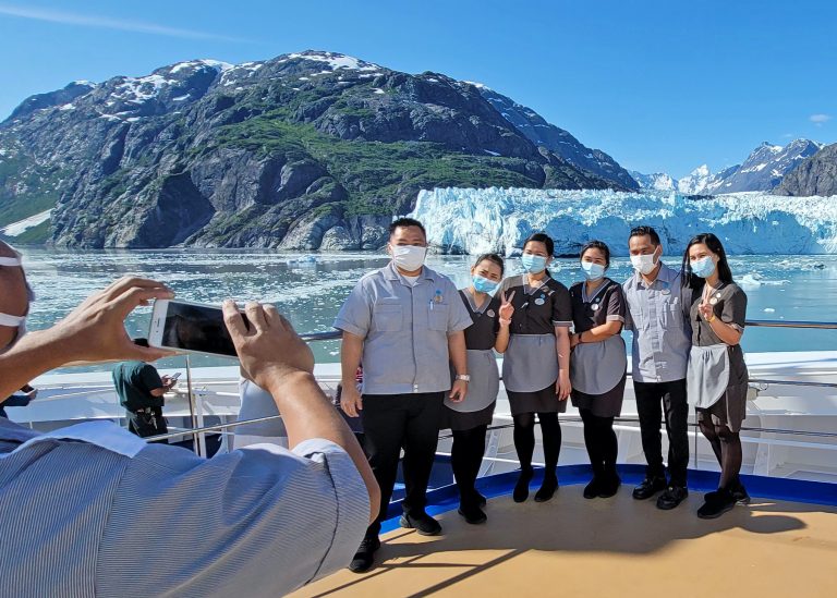 crew members get their picture taken in front a glacier while wearing masks
