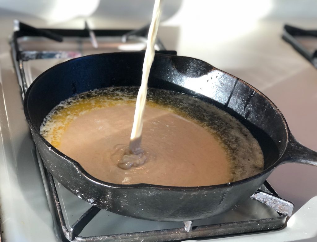 Liquid being poured into a cast-iron skillet that holds melted butter