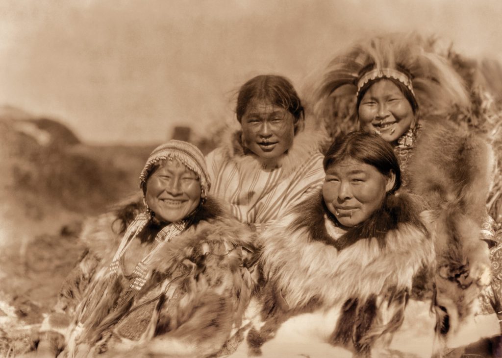 Four Alaska Native women smile and pose for this sepia photo.