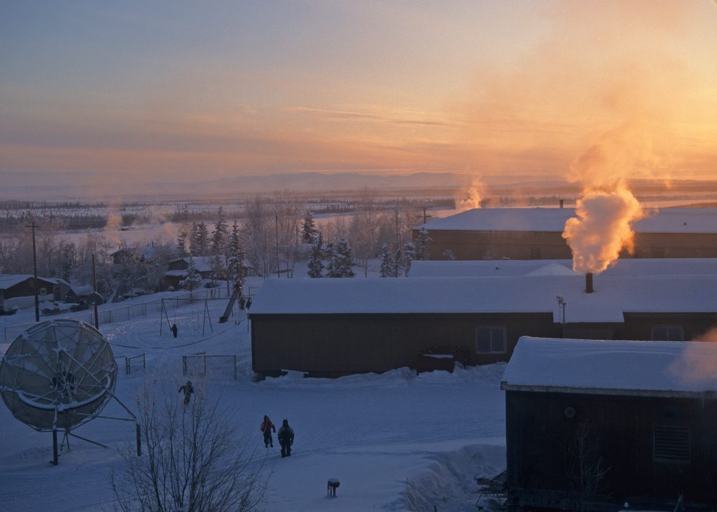 A glow of twilight lights snow-covered roofs with smoke billowing out of chimneys.
