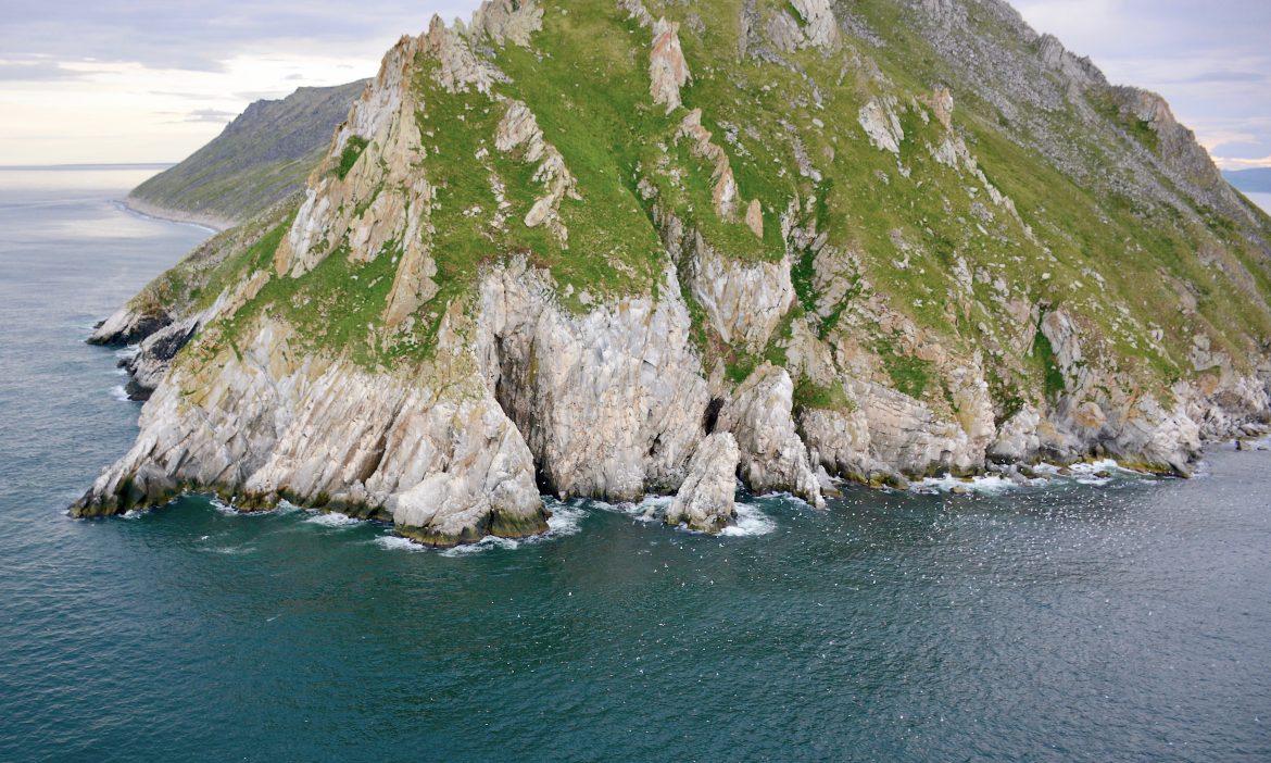 A rocky island with some greenery on more gradual slopes