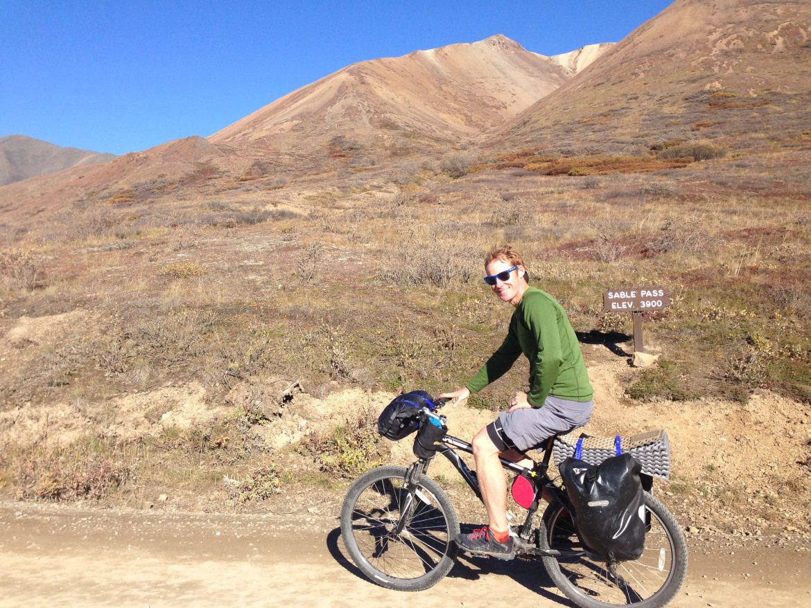 Man sits on bike on a sunny summer day. Bike on dirt road, short mountains behind
