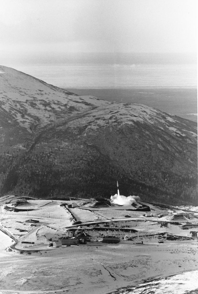Black and white photo of a missile launching from on top of a mountain