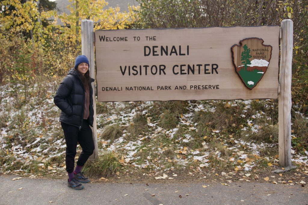 Woman poses next to Denali Visitor Center sign