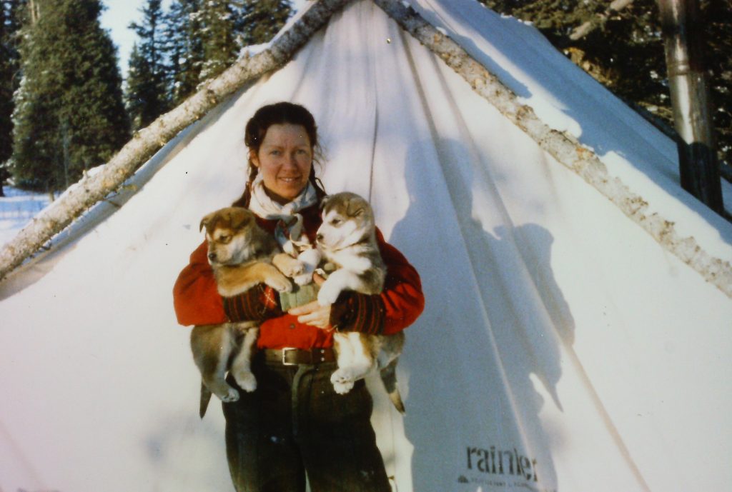 Woman standing in front of a tent holding puppies