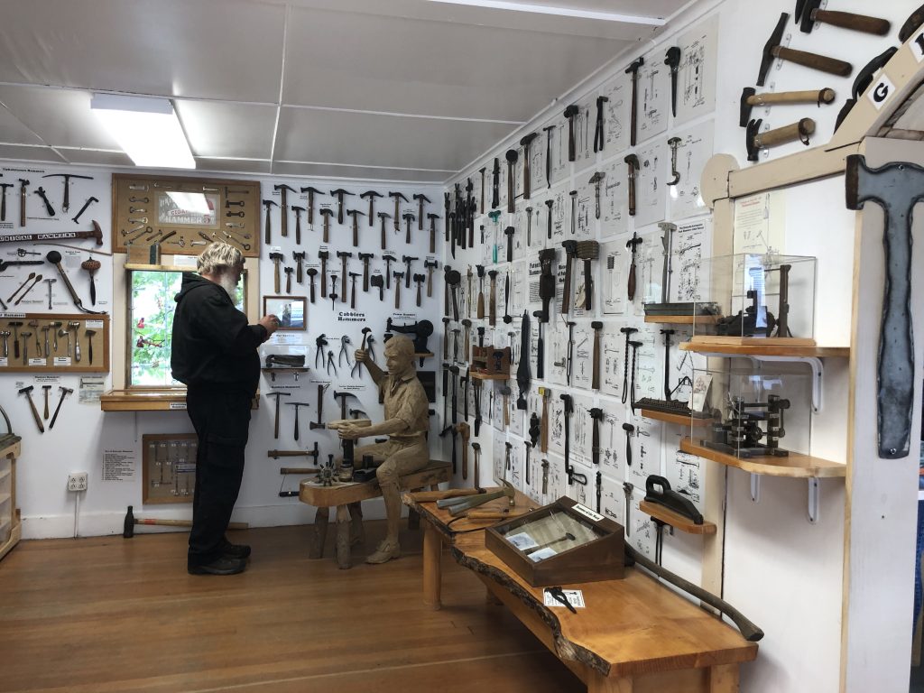 Man stands in the corner of a room with white walls that are covered with displays of different hammers.