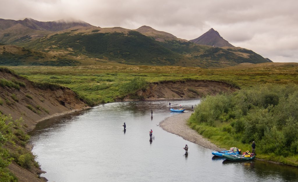 Anglers spread out and cast lines around a bend in the Goodnews River, slow-flowing water and mountains.