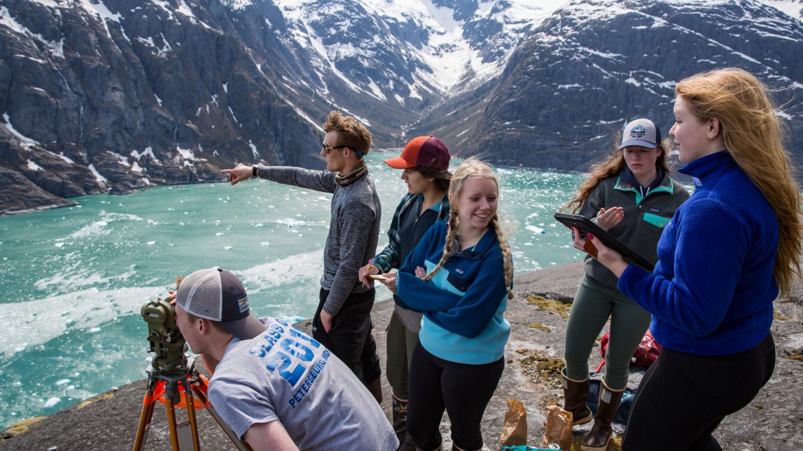 Students stand on rocky vantage point and use instruments to record data on LeConte Glacier