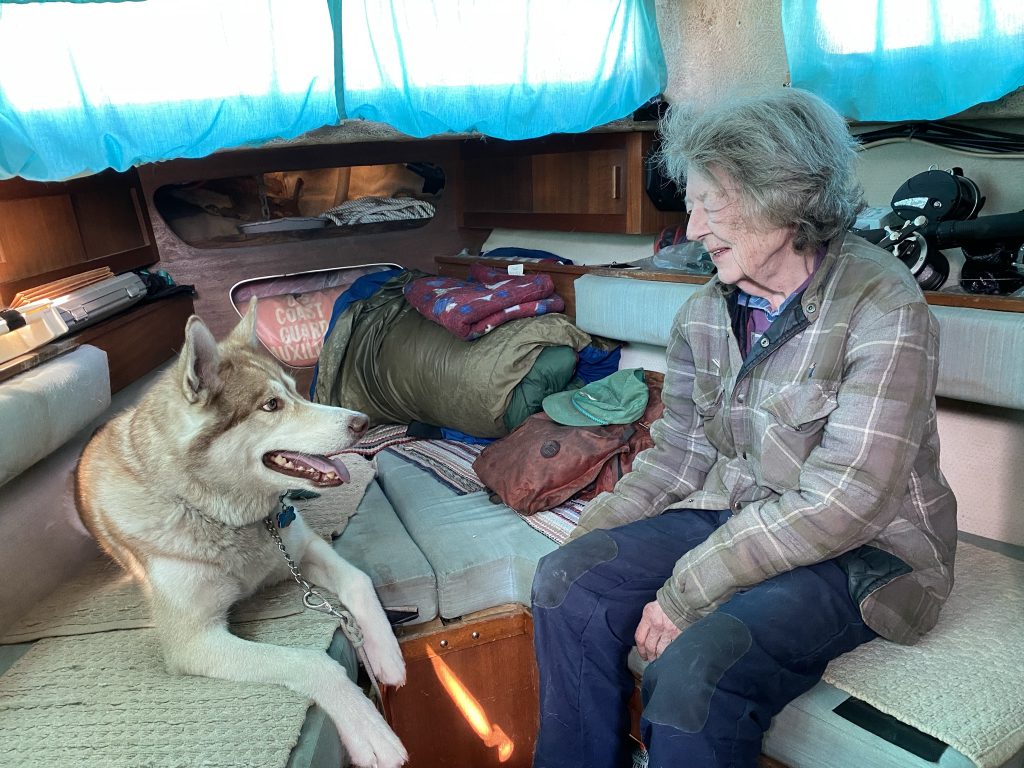 Lady sits on couch in boat with husky sitting across from her