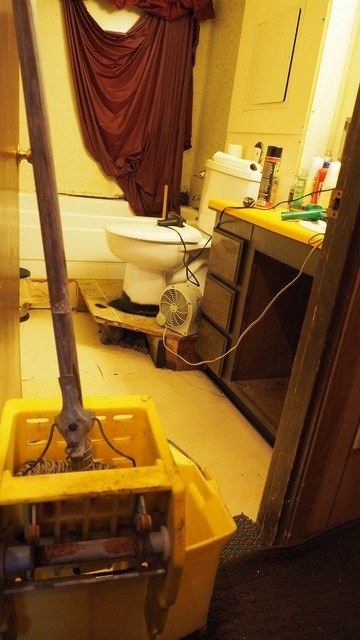 A small, dingy bathroom. Mop bucket ready to do necessary cleaning.